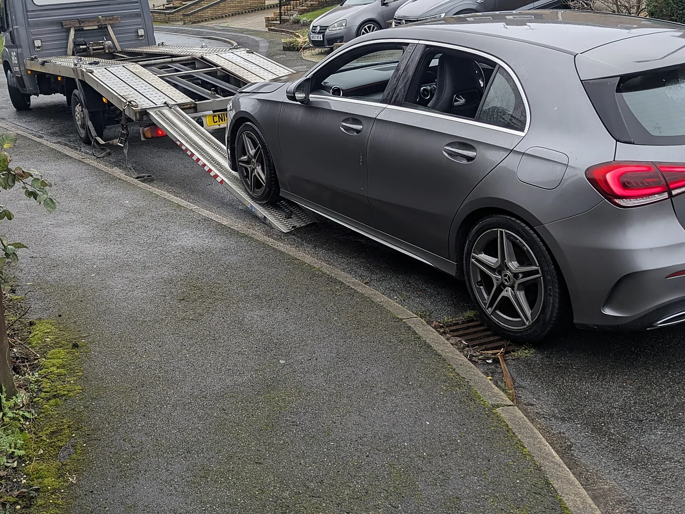 Recovery truck collecting a broken-down car on a British residential street, UK number plates visible